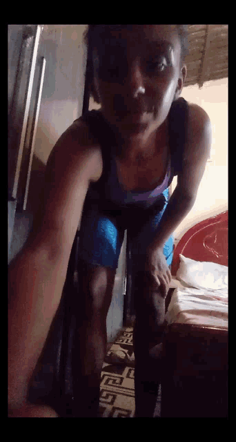 a woman in a purple tank top and blue shorts is standing in front of a bed