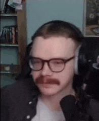 a man with glasses and a mustache is wearing headphones while sitting in front of a microphone .