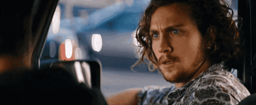 a man with curly hair and a beard is sitting in the driver 's seat of a car