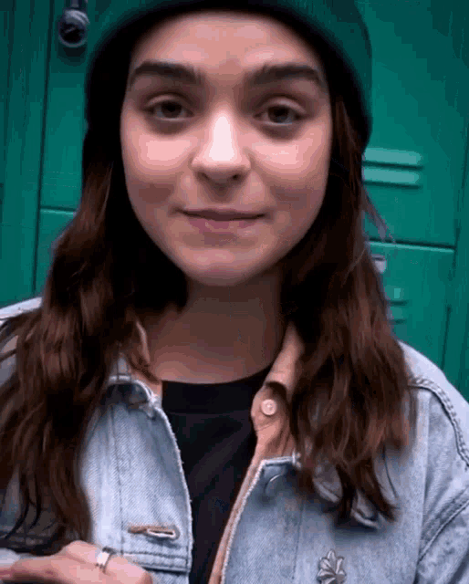 a girl wearing a beanie and a denim jacket is smiling