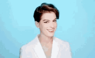a woman in a white jacket is smiling and looking down against a blue background .