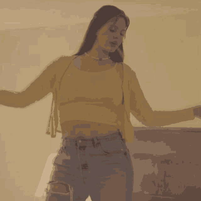 a woman wearing a yellow crop top and ripped jeans is dancing