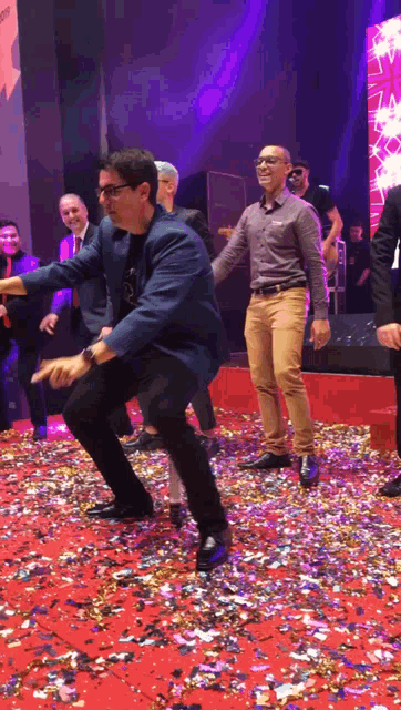a man in a blue jacket is dancing on a red carpet surrounded by confetti