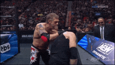 a wrestler is hugging another wrestler in front of a banner for aew dynamite
