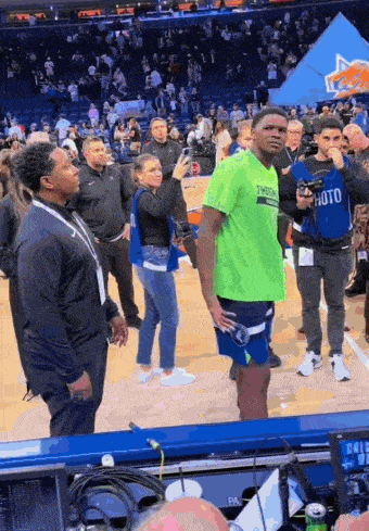 a man wearing a green shirt that says timberwolves stands on a basketball court