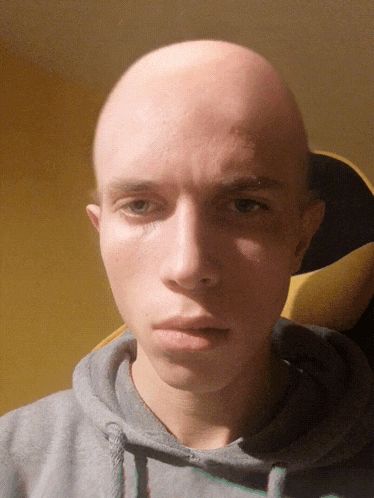 a man with a bald head is wearing a gray hoodie