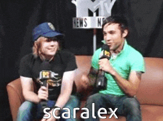 two men are sitting on a couch and one of them is holding a microphone and the word scaralex is on the bottom