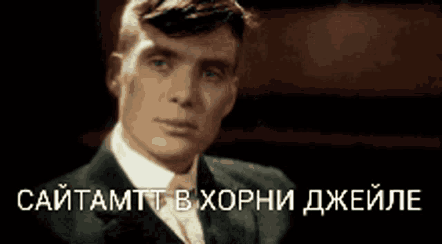 a man in a suit and tie is looking at the camera with a foreign language caption behind him