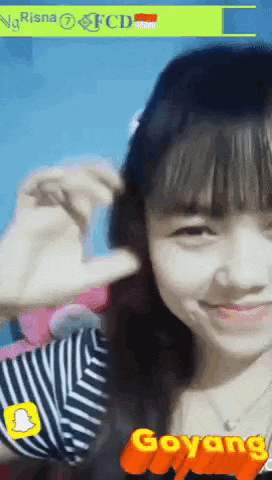 a girl in a striped shirt is smiling and making a heart with her hands .