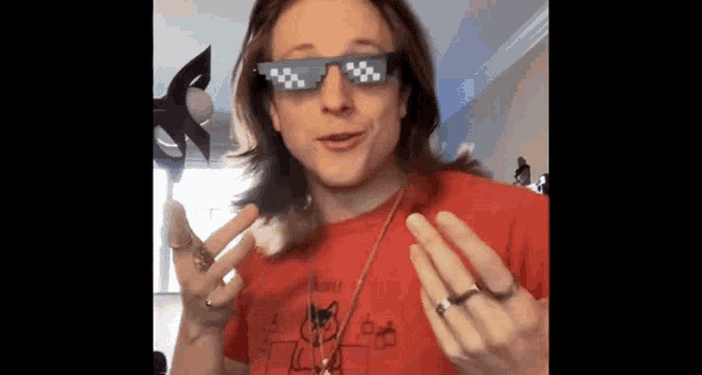 a man wearing sunglasses and a red shirt with a cat on it is giving a peace sign