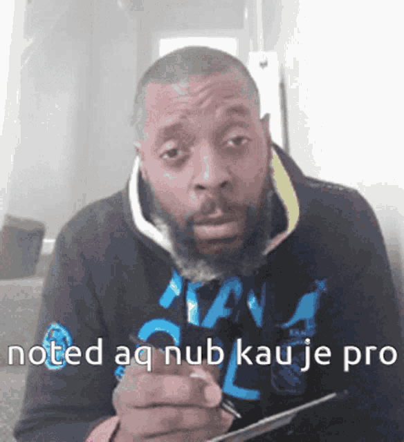 a man with a beard is writing on a piece of paper with the words " noted aq nub kau je pro " on the bottom