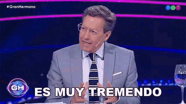 a man in a suit and tie is sitting in front of a sign that says es muy tremendo