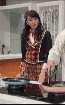 a woman in a plaid dress is standing next to a man holding a frying pan