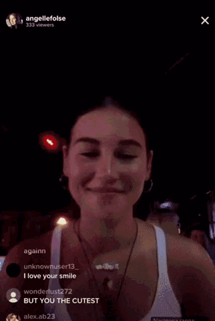 a woman in a white tank top is smiling in front of a red light and says " but you 're cutest "
