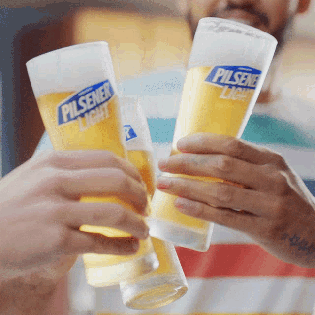 two glasses of pilsener light beer are being held by a man