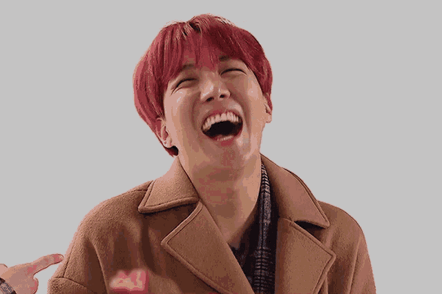 a young man with red hair is laughing and wearing a brown coat