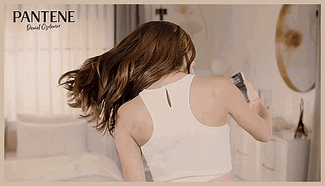 a woman in a white tank top is holding a bottle of pantene shampoo