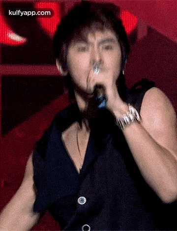 a man is singing into a microphone with the words kulfyapp.com visible in the corner
