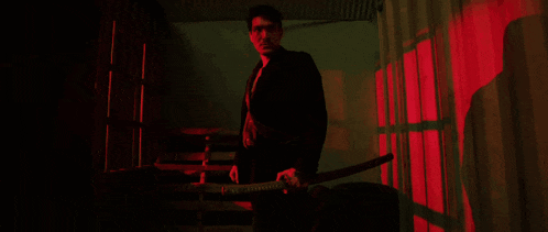 a man stands in a dark room with red lights behind him