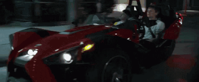 a man and woman are riding a red slingshot on a street at night