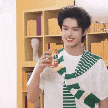 a man wearing a green and white striped scarf holds a can of orange soda