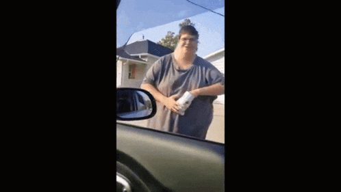 a very fat man is standing in front of a garage in a car .