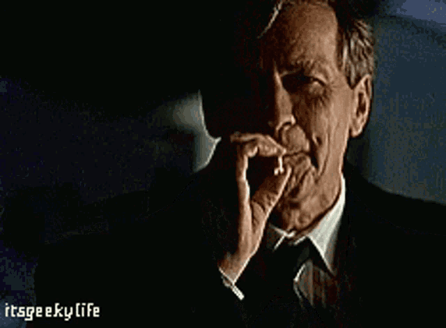 a man in a suit and tie is smoking a cigarette with the words itsgeekylife below him