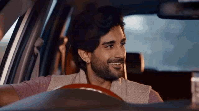 a man with a beard is smiling while sitting in the driver 's seat of a car
