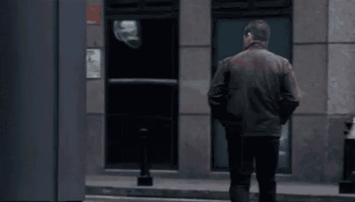 a man in a brown jacket is standing in front of a building .