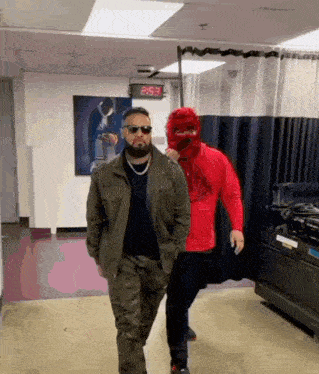 two men are walking in a hallway with a digital clock that says 2:53