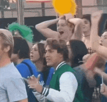 a man in a green jacket is standing in a crowd of people holding balloons .