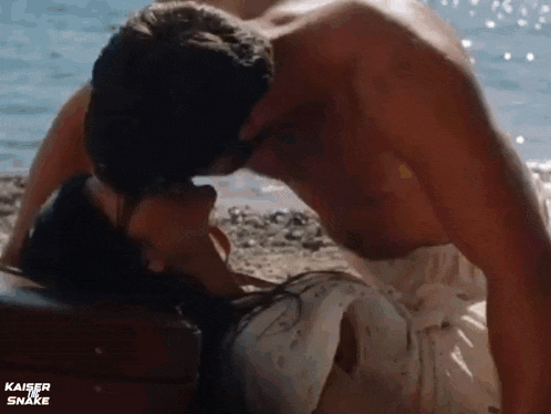 a man and a woman are kissing on a beach near the water .
