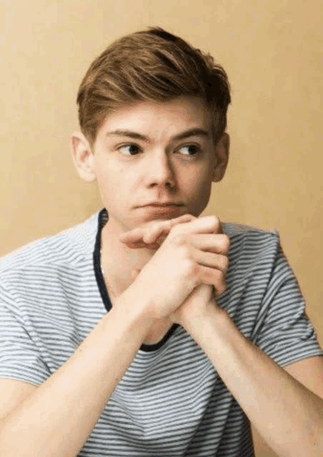 a young man in a striped shirt is sitting with his hands folded