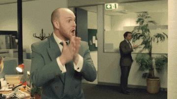 a man in a suit and tie is clapping in an office with a green exit sign in the background