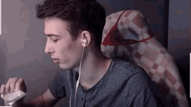 a young man wearing headphones is sitting in a chair and holding a remote control .
