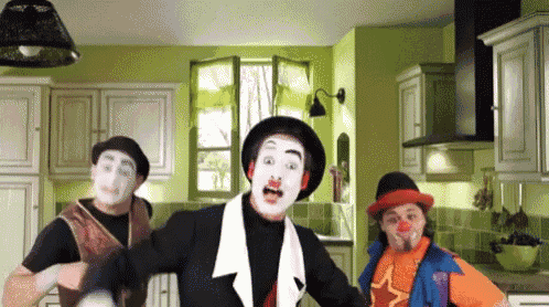two clowns are dancing in a kitchen and one is wearing an orange vest