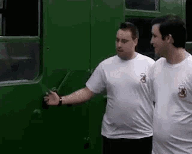 two men are standing next to each other in front of a green vehicle .