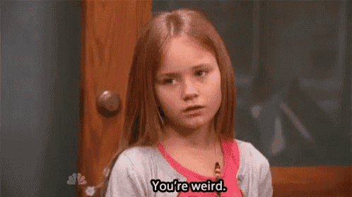 a young girl is standing in front of a door and saying `` you 're weird '' .