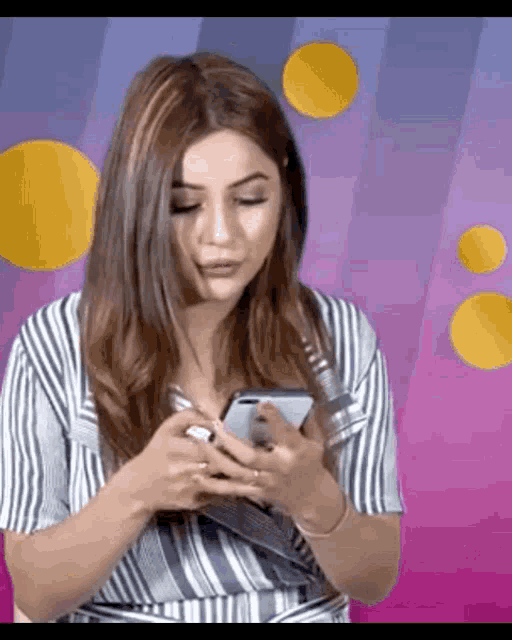 a woman in a striped shirt is holding a cell phone in her hand .