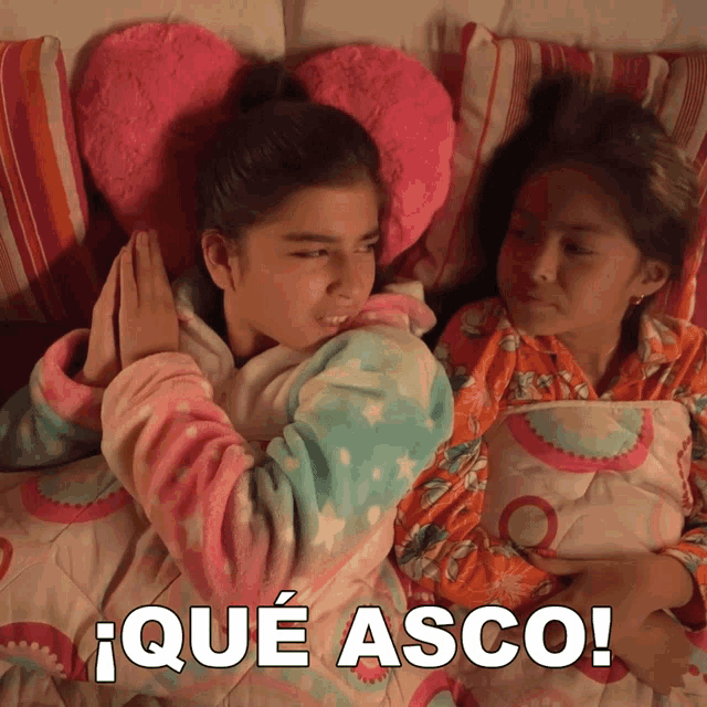 two girls laying on a bed with the words que asco