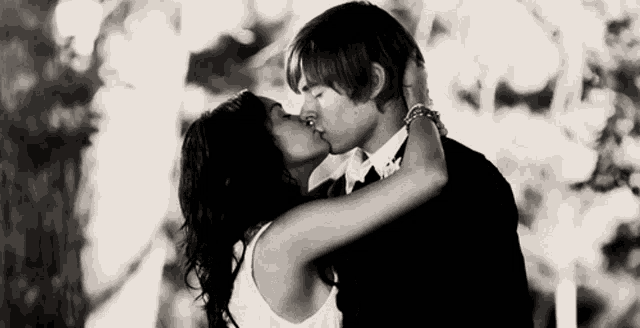 a man and a woman kissing in front of trees