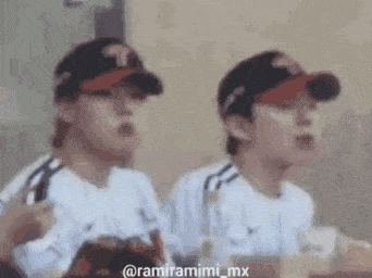 two men wearing baseball caps are sitting next to each other in a restaurant .