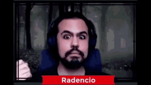 a man with a beard and headphones is making a funny face in front of a forest .