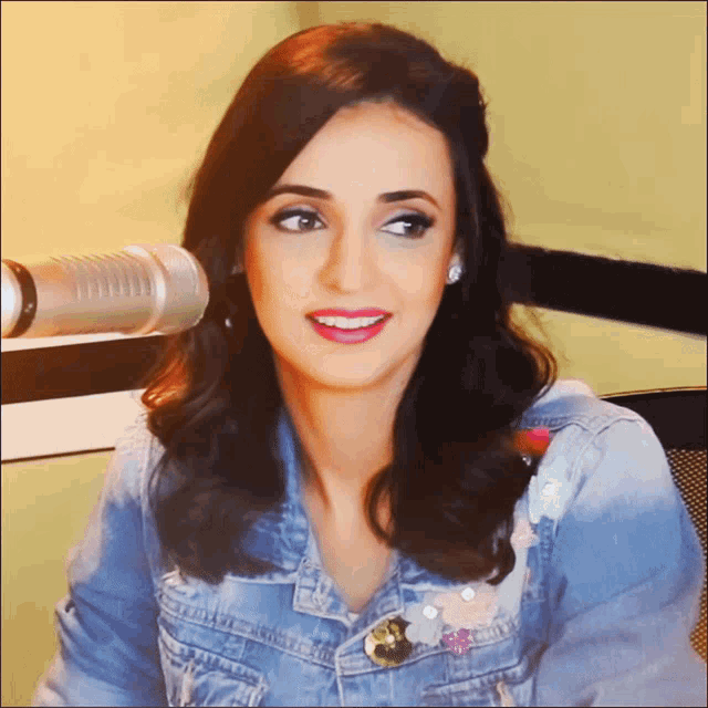 a woman in a denim jacket is sitting in front of a microphone and smiling