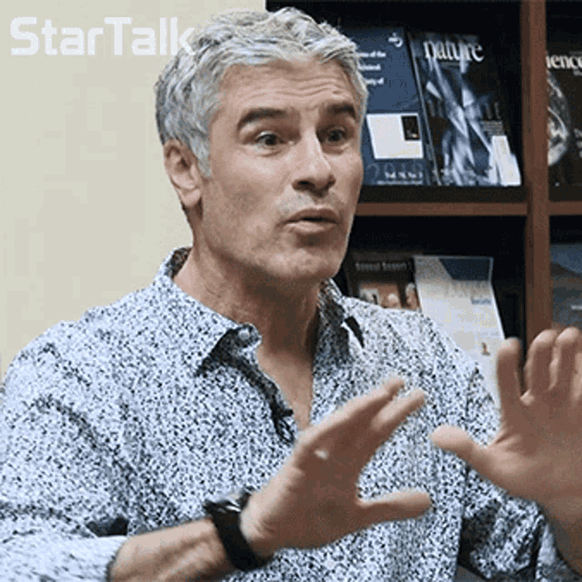 a man talking in front of a shelf with books including nature