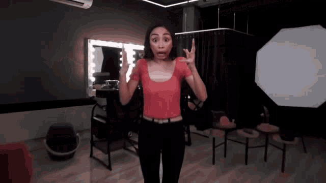 a woman in a red top is standing in front of a mirror making a funny face