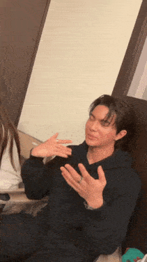 a man in a black hoodie is sitting on a couch making a funny face .