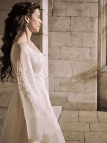 a woman in a white dress is standing in front of a stone wall