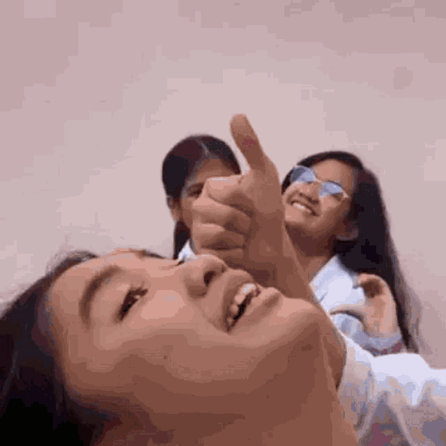 a girl is giving a thumbs up sign while another girl looks on and smiles .
