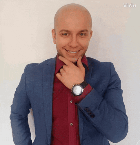 a bald man wearing a blue suit and a red shirt has a watch on his left wrist
